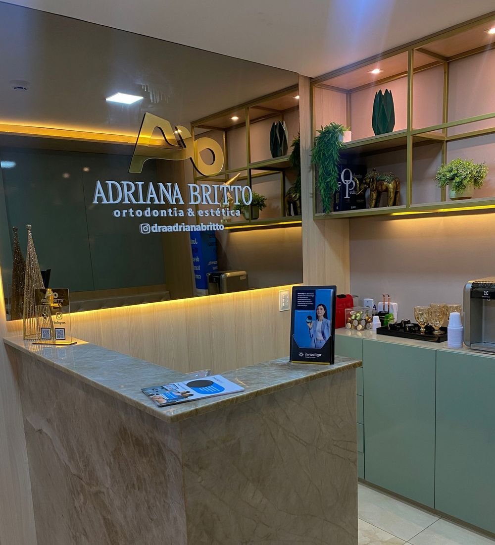 Recepção da clínica com o logo Adriana Britto Ortodontia & Estética na parede